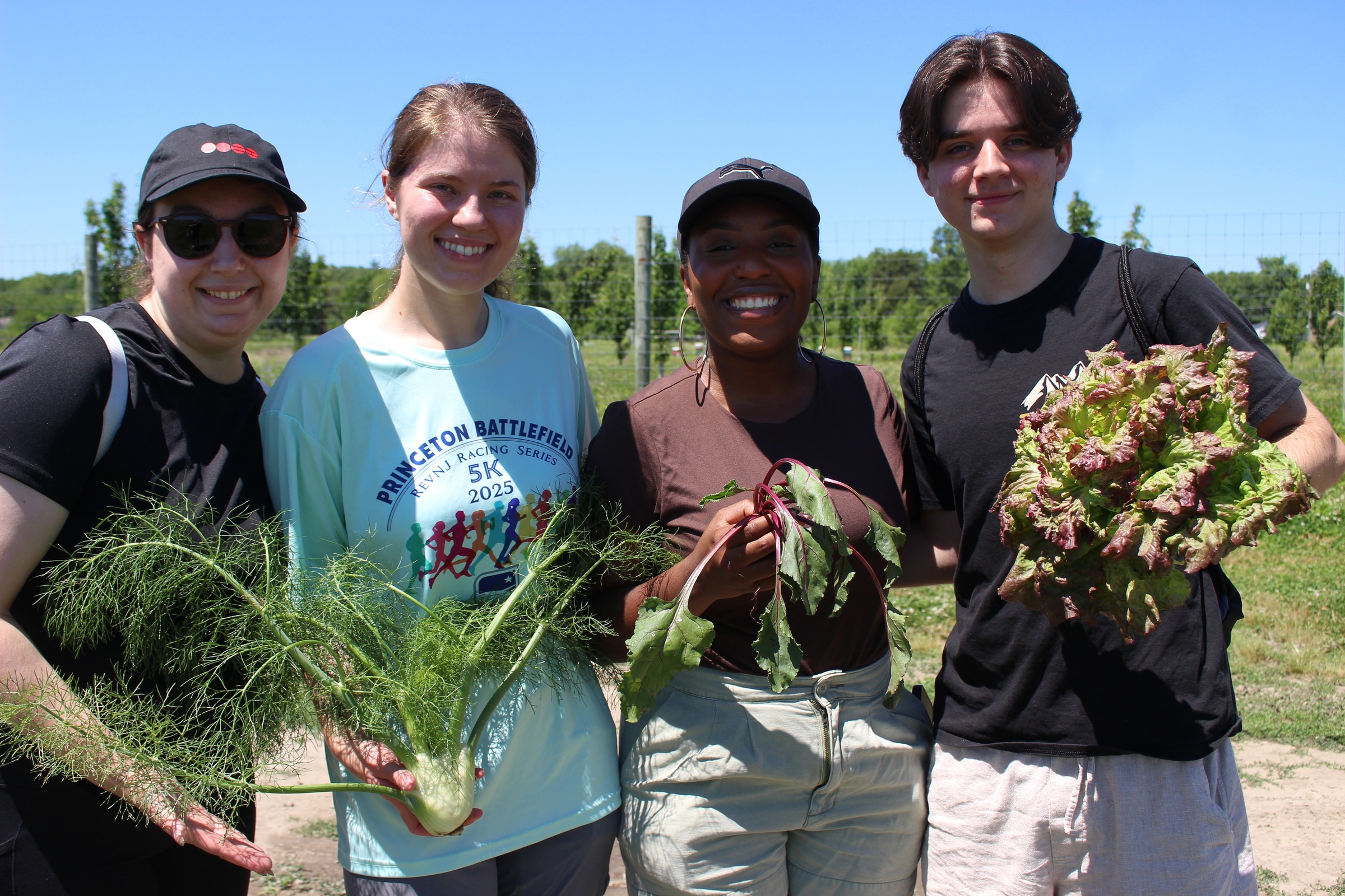 Four smiling people stand together holding fennel, a beet with leaves and a large head of lettuce.