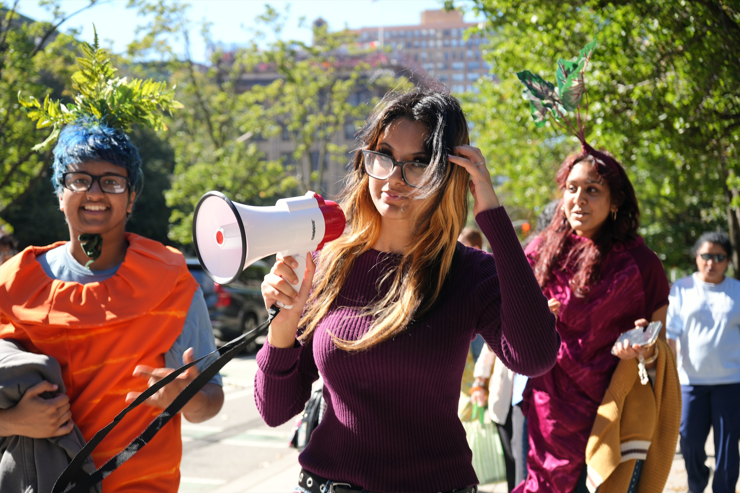 A participant holds a megaphone between marchers wearing carrot and beet costumes.
